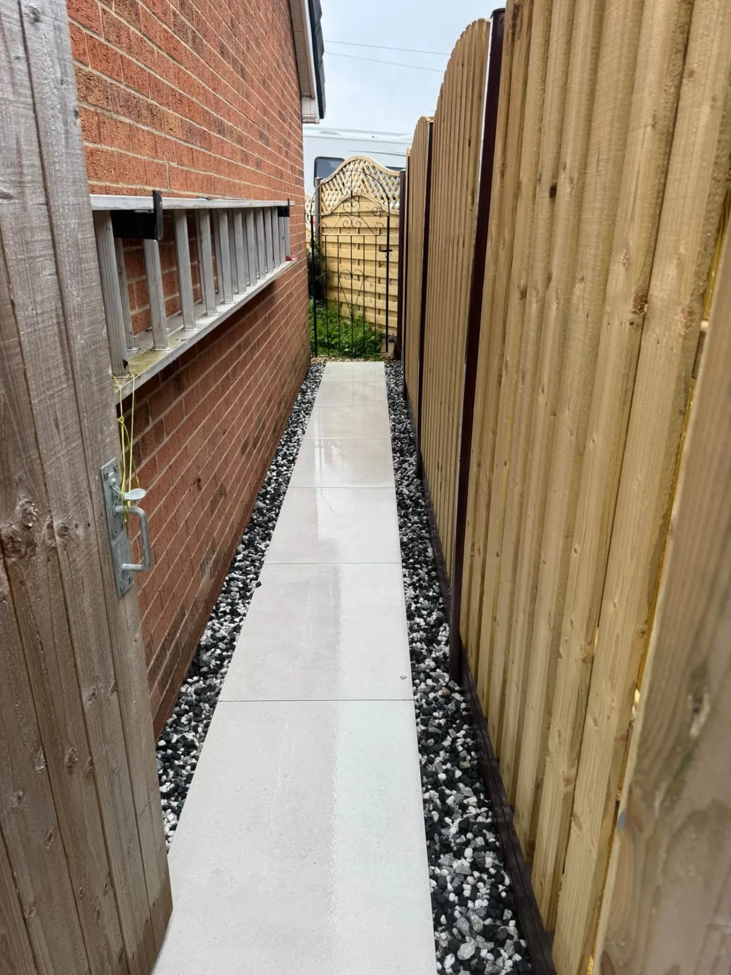 Narrow porcelain side path with gravel edging beside a timber fence