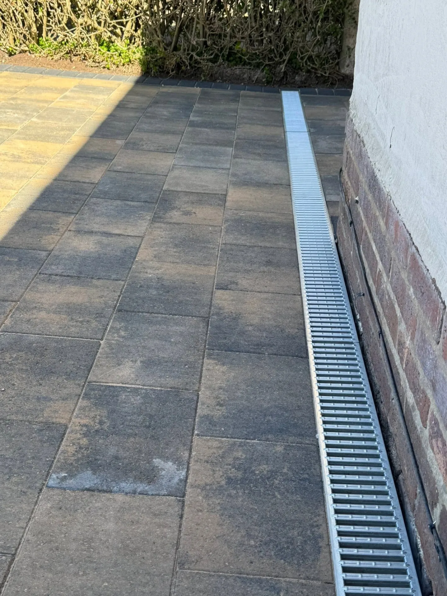 Dark block paving with a linear drainage channel beside a house