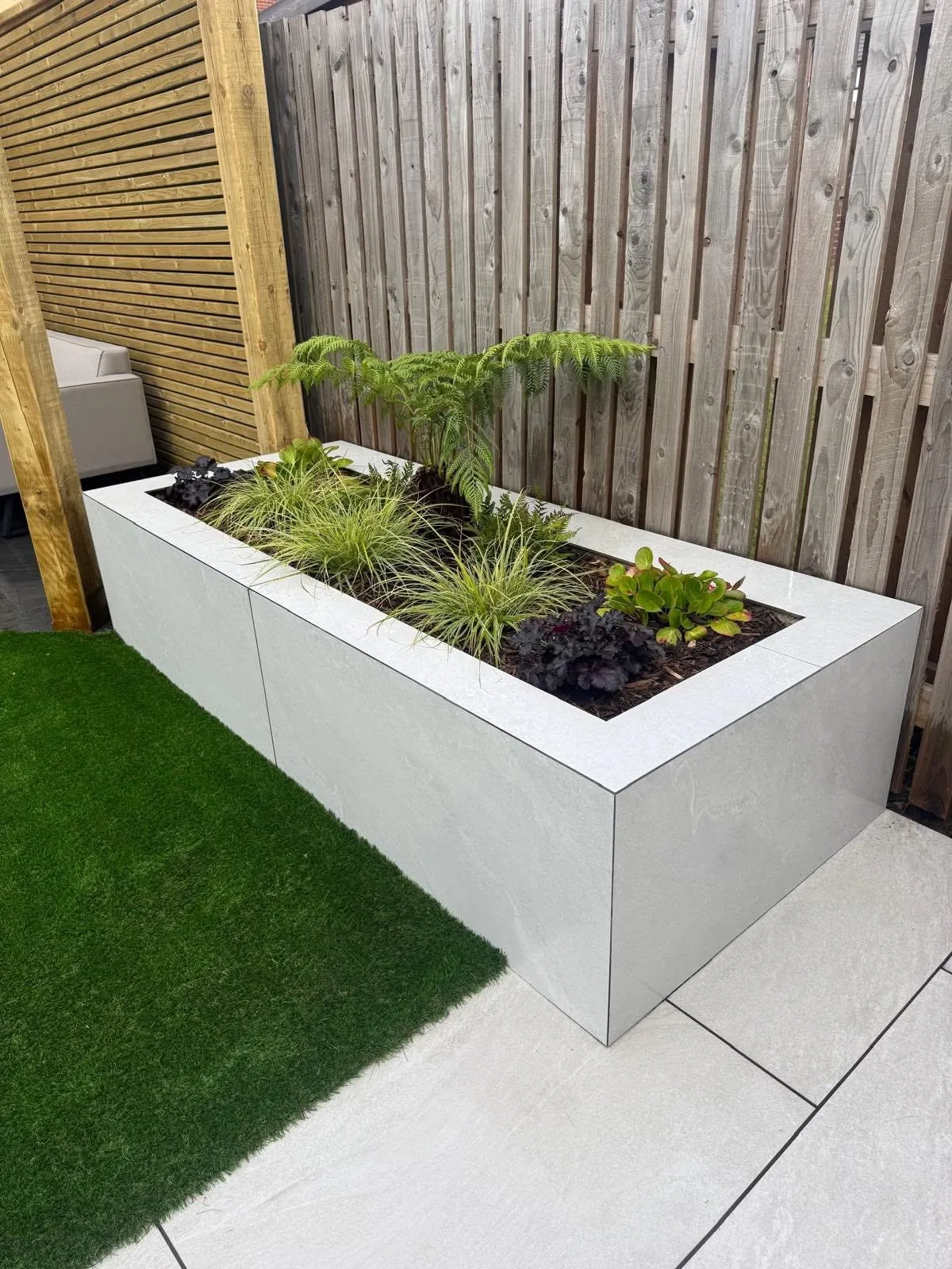 Rendered raised planter beside artificial grass and porcelain paving