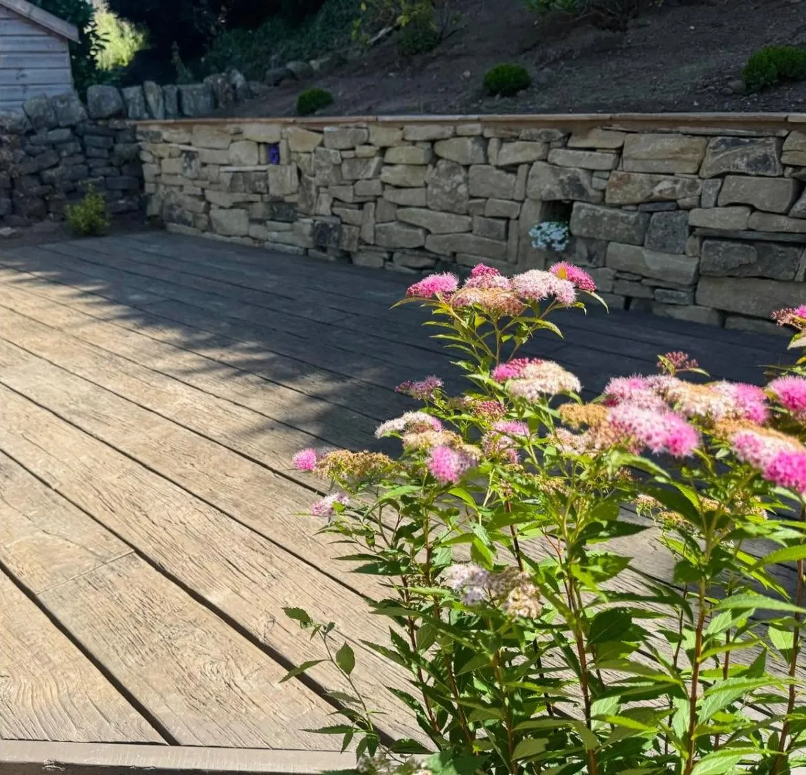 Decking beside a stone retaining wall with flowering plants