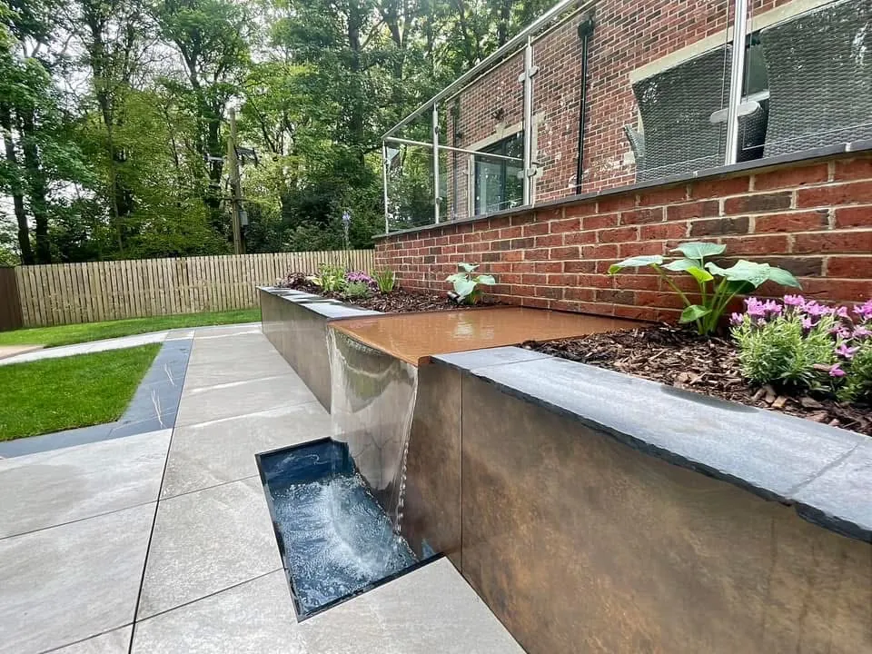 Corten steel water blade falling into a rill beside porcelain paving