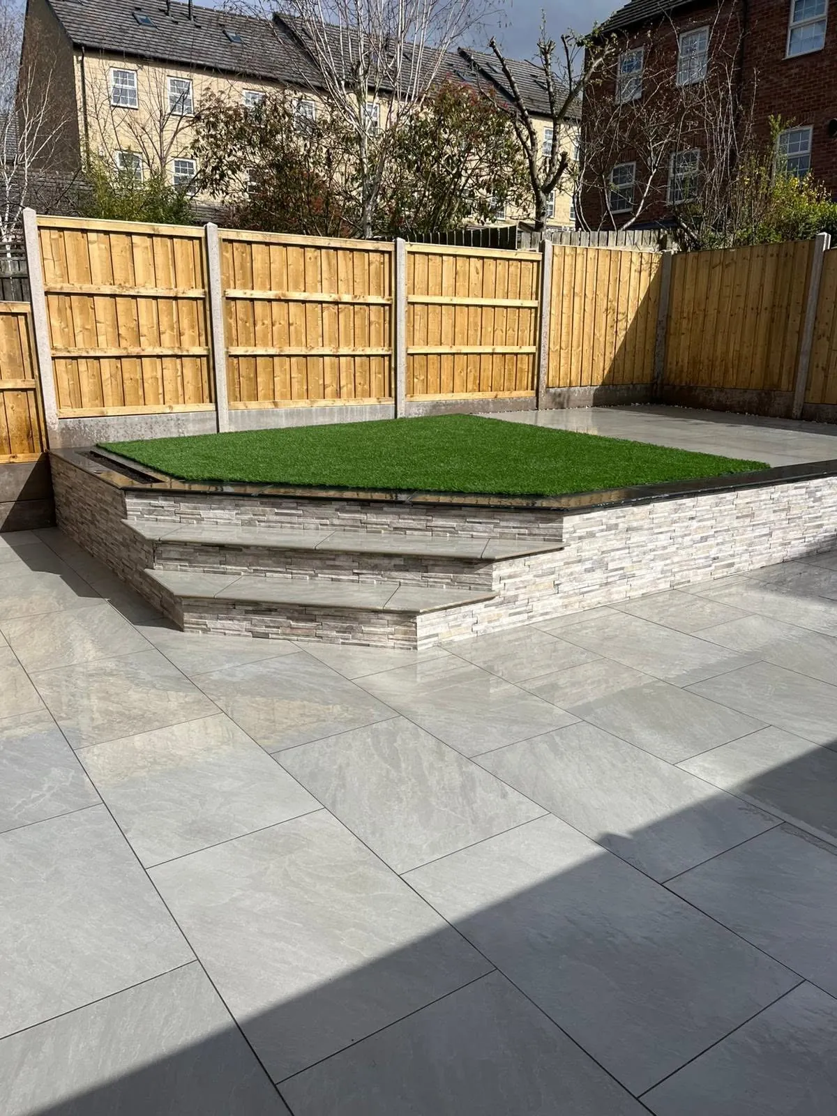 Porcelain patio with steps up to a raised artificial lawn