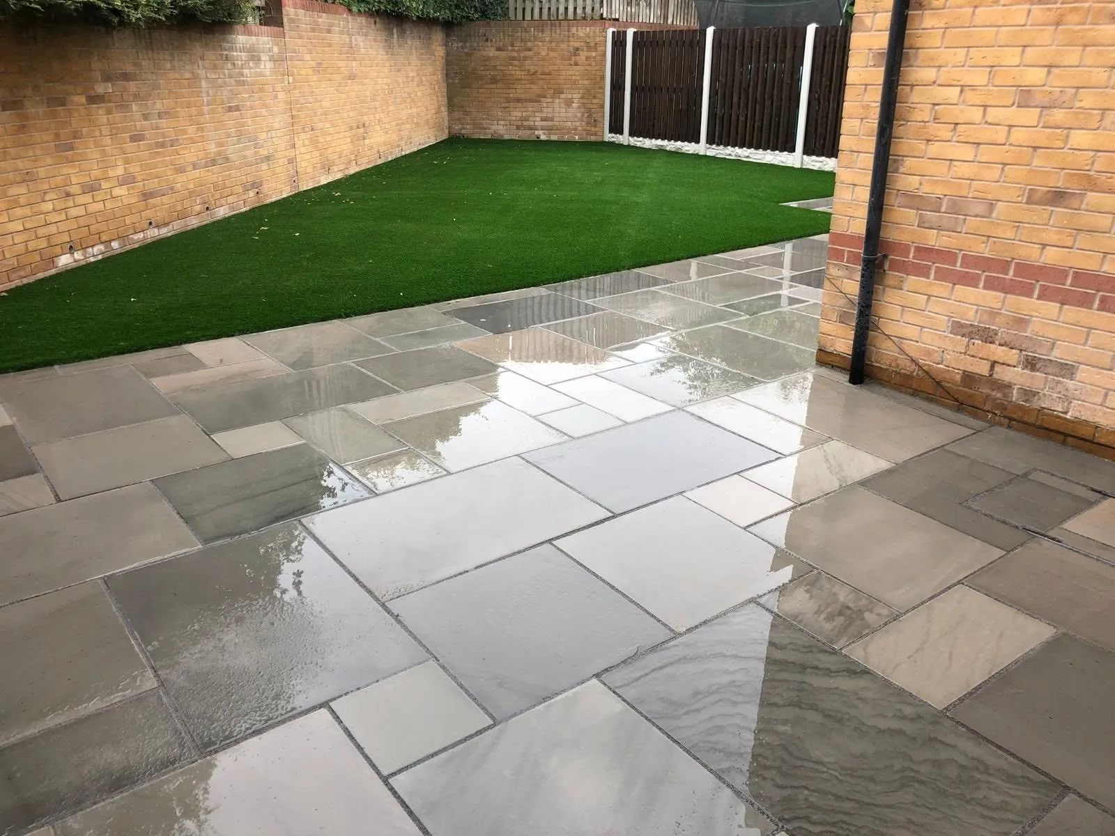 Grey porcelain patio leading to an artificial lawn in a walled garden