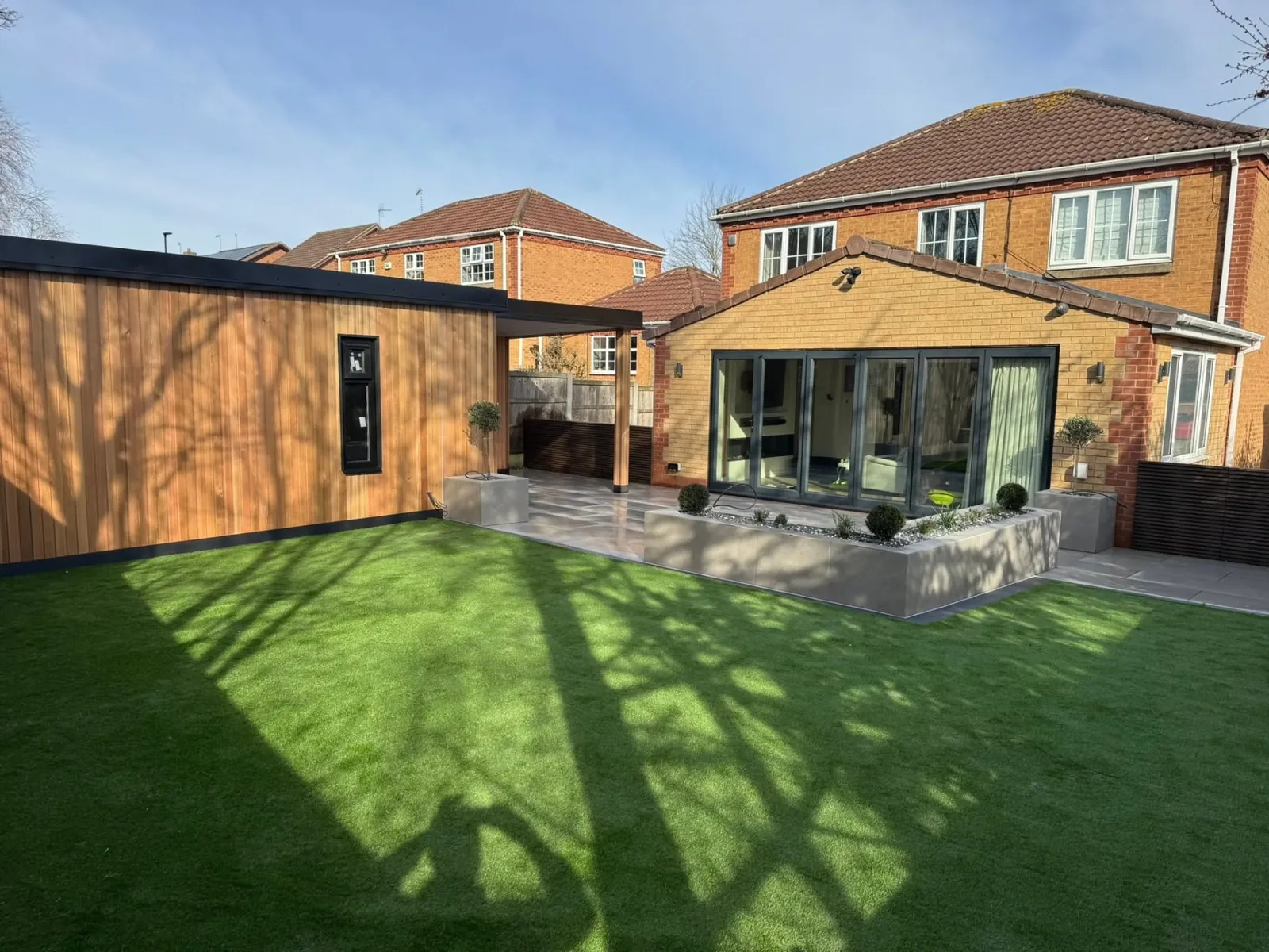 Timber-clad garden room beside a patio and lawn