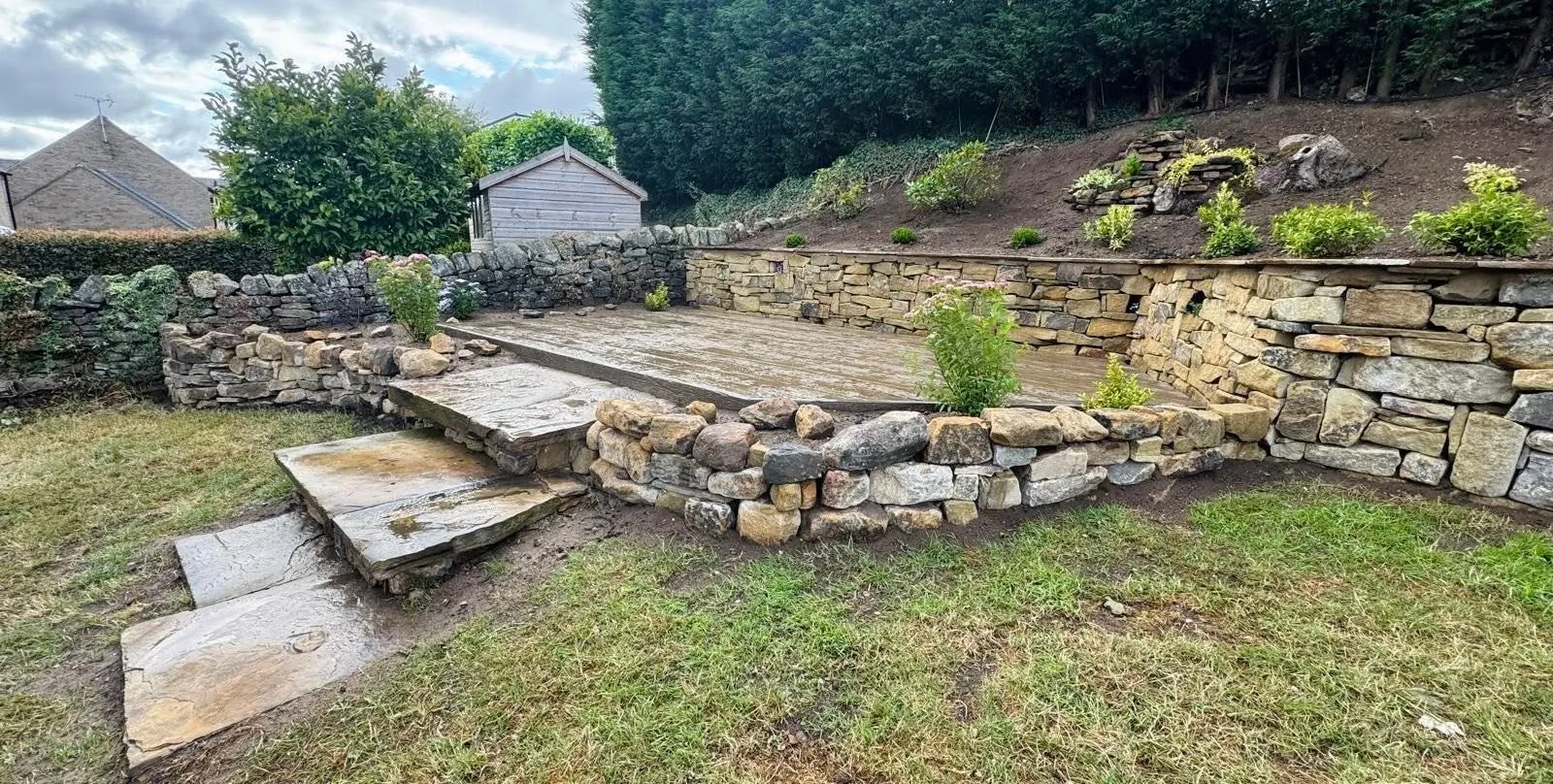 Terraced sloping garden with stone walls, steps and a raised deck