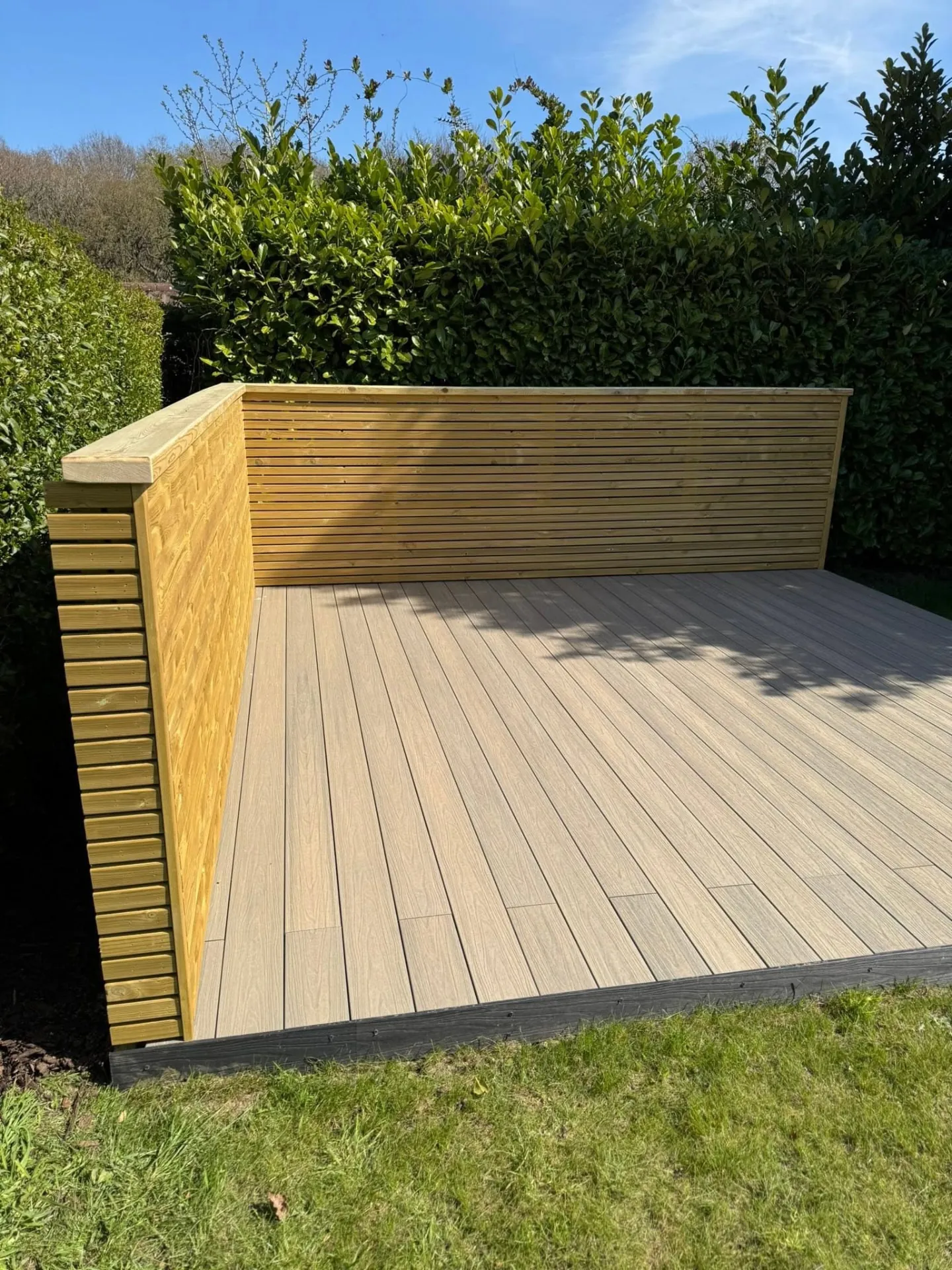 Corner composite deck with matching slatted screen against a hedge