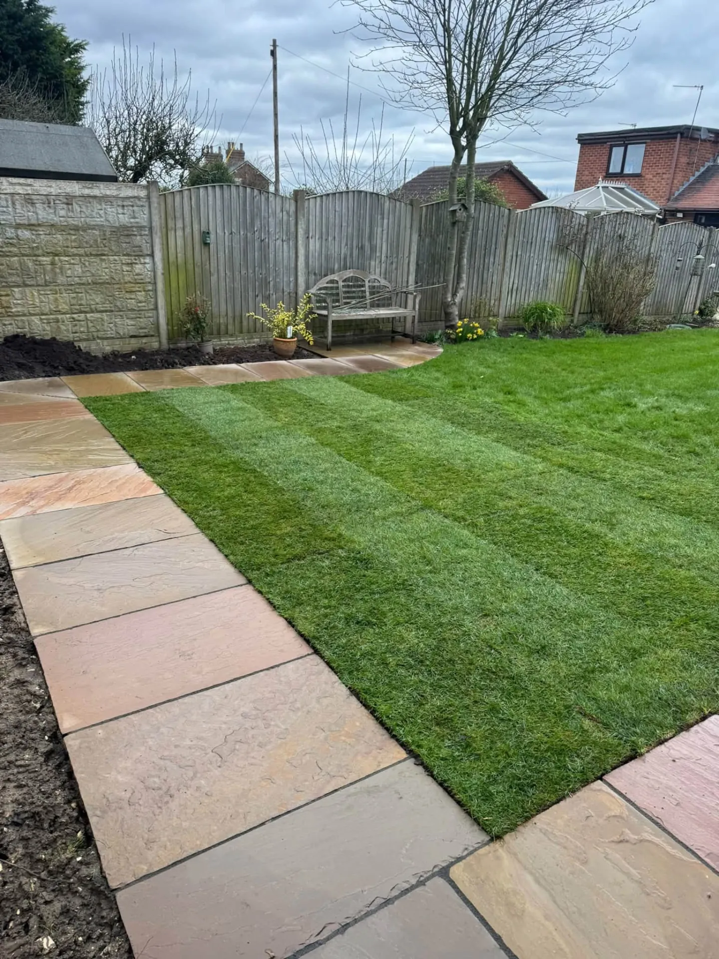 New turf lawn with paved border and timber fence