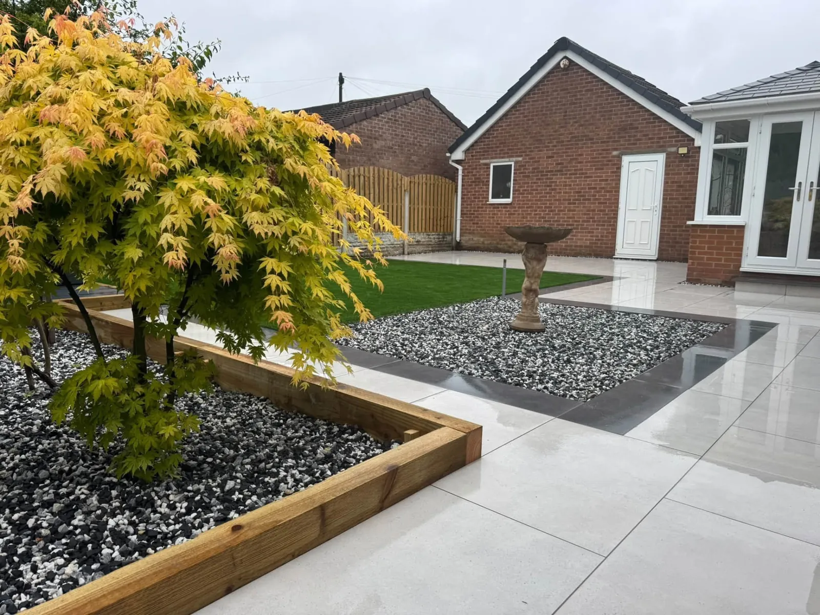 Porcelain patio with gravel bed and timber-edged planter beside a bungalow