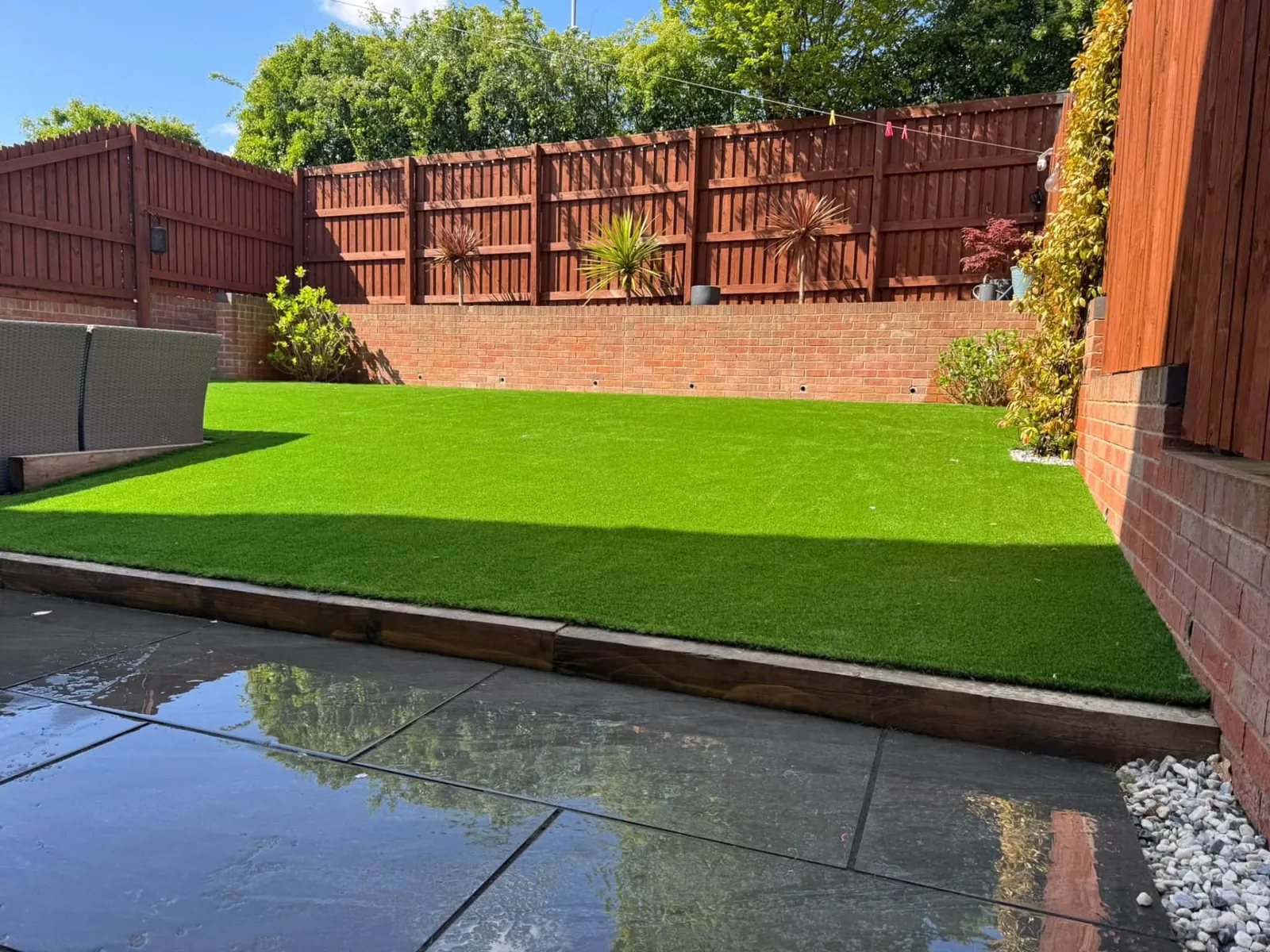 Artificial grass lawn above a dark paved patio with brick retaining walls