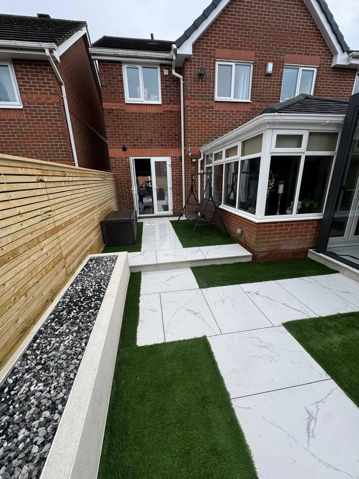 Artificial grass strips between pale tiled paths in a narrow modern garden