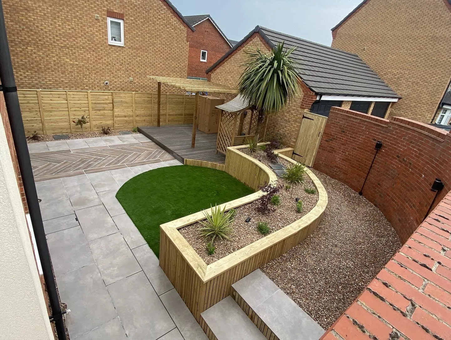 Courtyard garden with curved timber sleeper planter, artificial lawn and pale paving