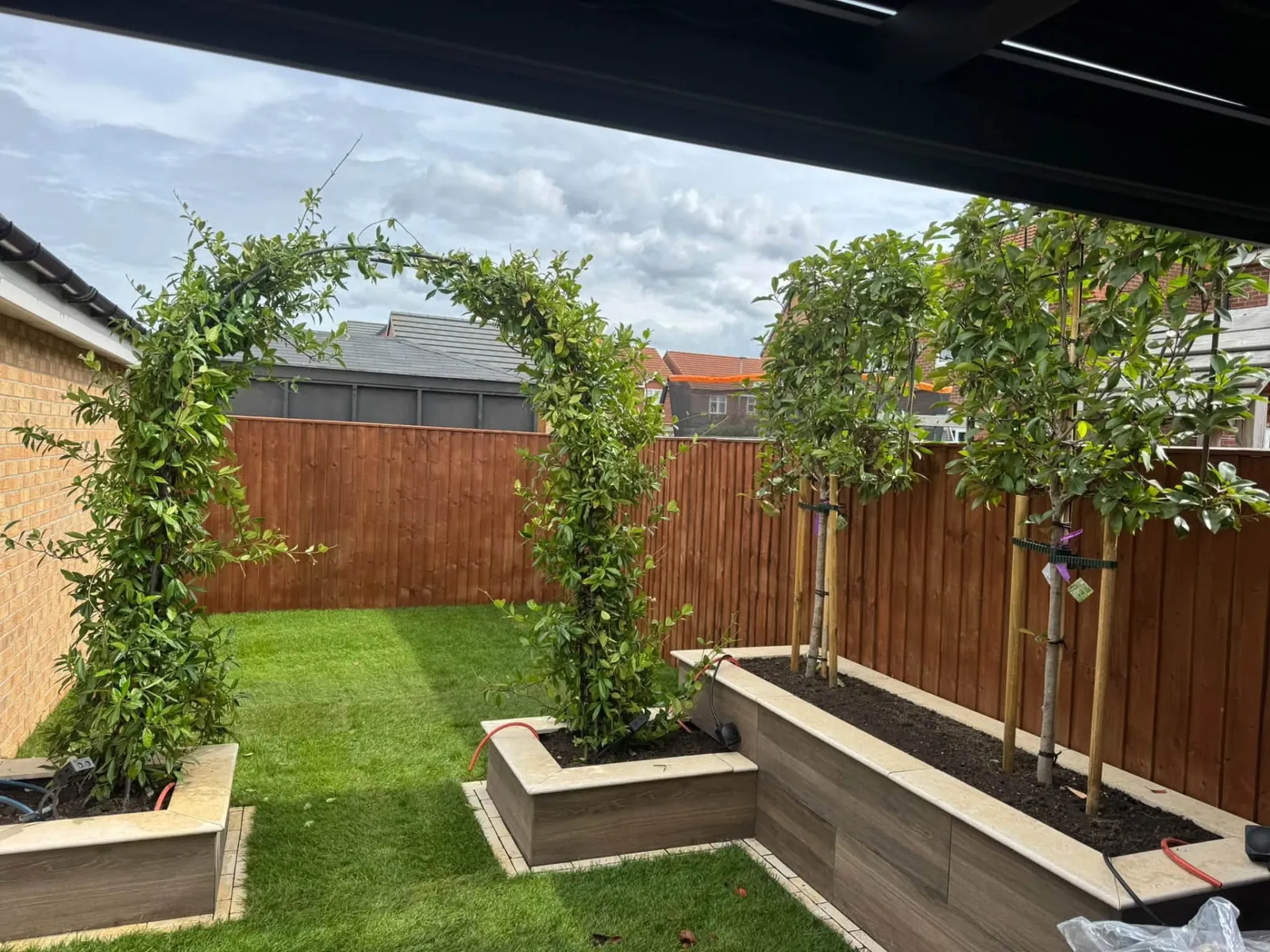 Raised timber planters with climbing plant arches around a lawn