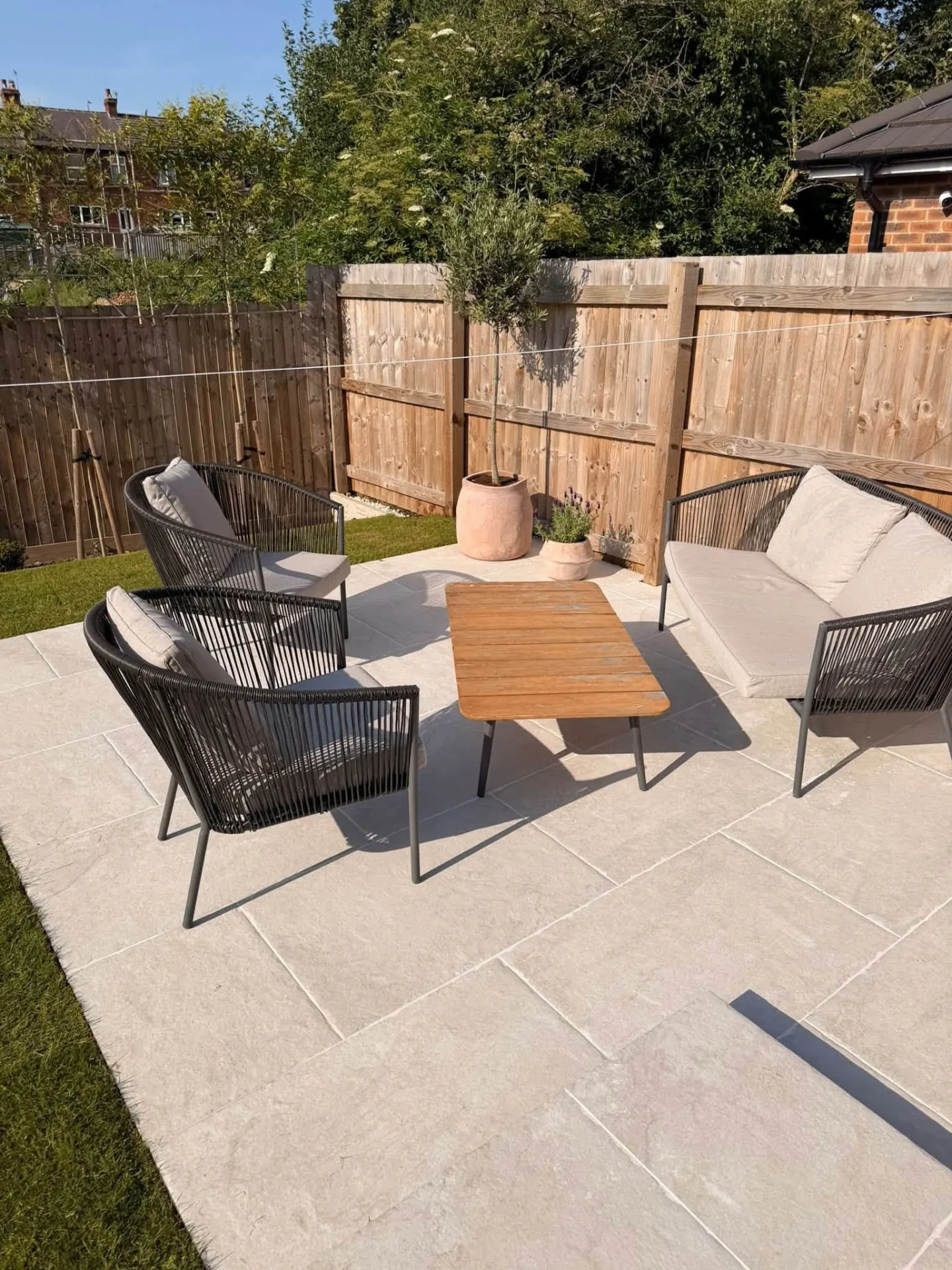Pale sandstone patio with outdoor sofa set in a fenced garden