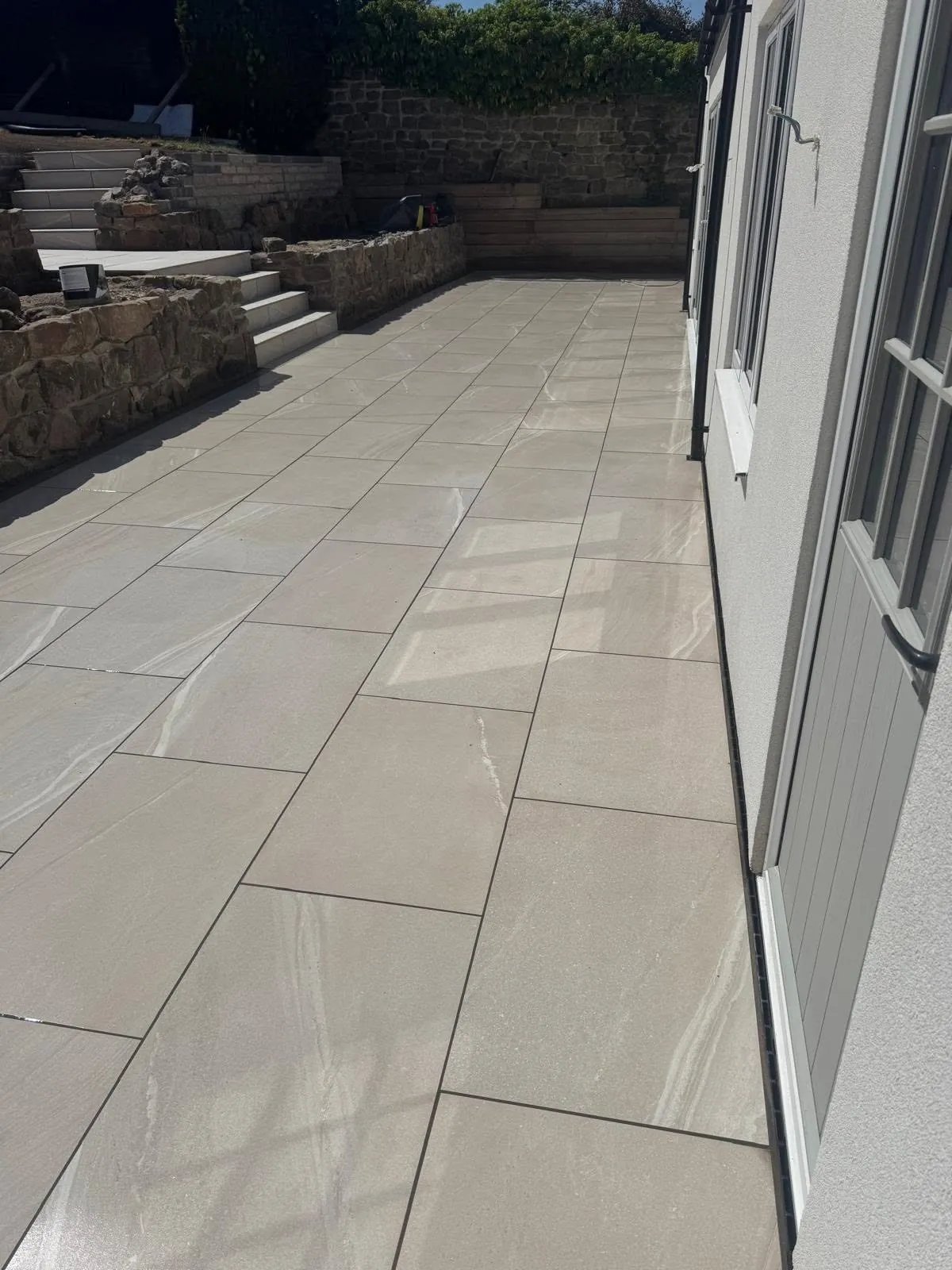 Porcelain patio being laid beside a house with stone walls behind
